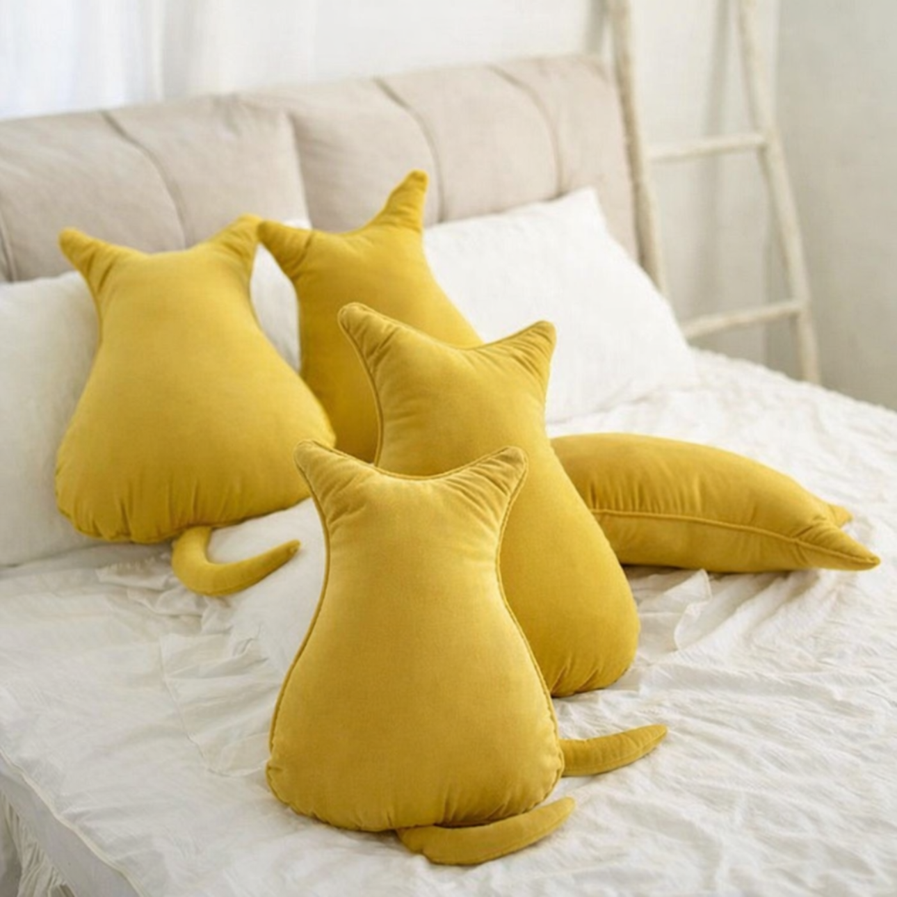 Yellow cat-shaped cushions on a bed with a neutral background